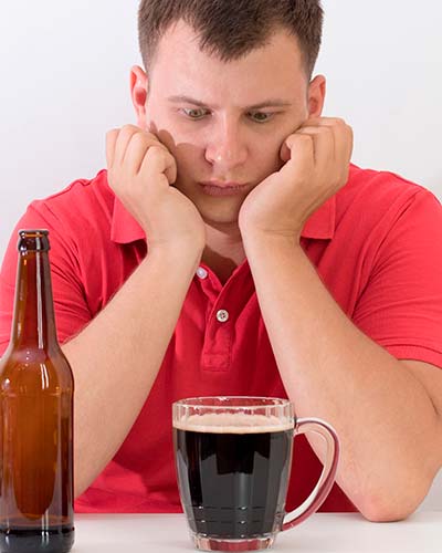 грустный мужчина сидит за столом перед кружкой с пивом